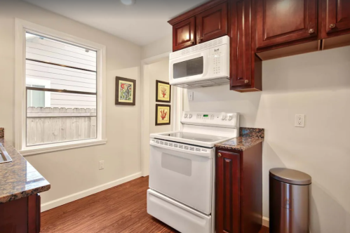 A modern kitchen featuring dark wood cabinets, a white stove, and a microwave, with a window and decorative wall art.