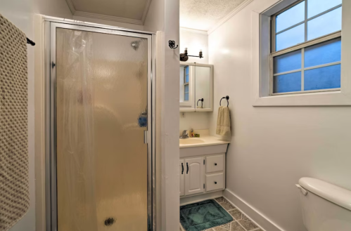 A clean bathroom featuring a shower, sink with mirror, and toilet, with a window allowing natural light.