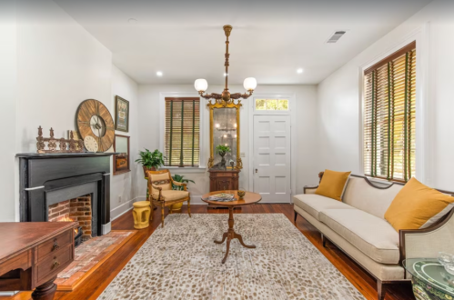Cozy living room with a fireplace, vintage decor, a round table, and a sofa with yellow cushions on a patterned rug.