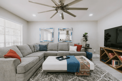 Cozy living room with a gray sectional sofa, decorative pillows, a coffee table, and a large TV on a wooden stand.
