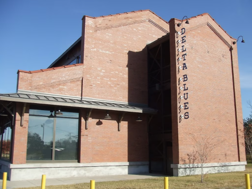 Exterior of the Delta Blues building, featuring a brick facade and large windows under a clear blue sky.