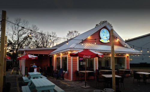 A cozy restaurant with outdoor seating, string lights, and umbrellas, set against a twilight sky.