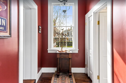 A hallway with red walls, a window, and a small table with a decorative item, featuring a patterned runner.