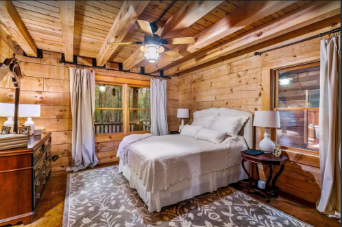 Cozy wooden bedroom with a bed, nightstands, and large windows, featuring rustic decor and warm lighting.