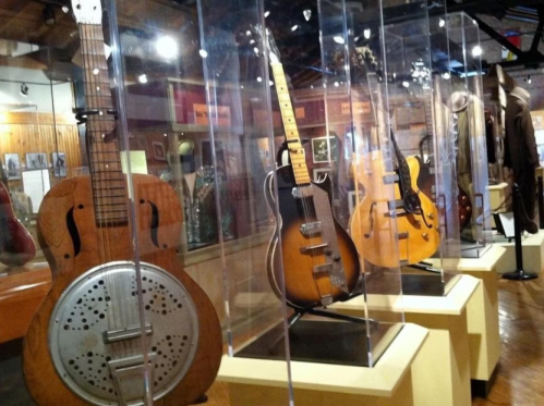 A display of vintage guitars in a museum, showcasing various styles and designs behind glass cases.