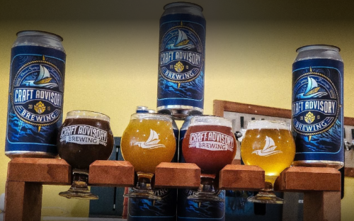 A display of various craft beers in cans and glasses, featuring the Craft Advisory Brewing logo.