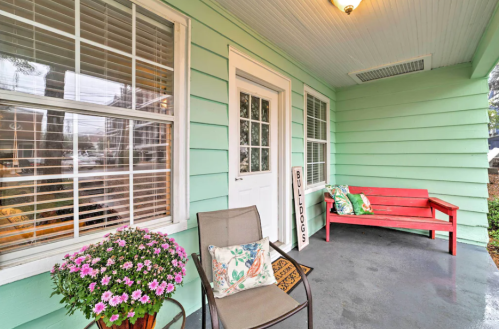 A cozy porch with a red bench, chair, potted flowers, and a sign reading "BULLDOGS" against a mint green wall.