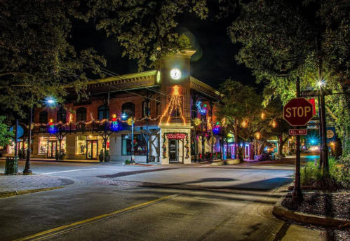 A charming brick building with a clock, adorned with lights, at night in a lively street scene.