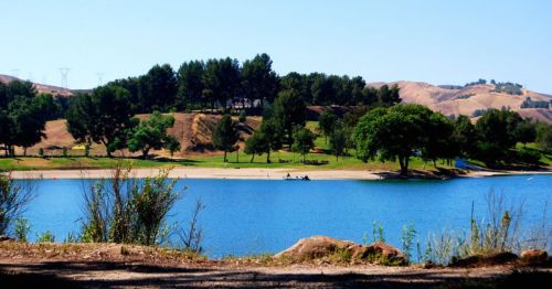 A serene lake surrounded by green trees and rolling hills under a clear blue sky.