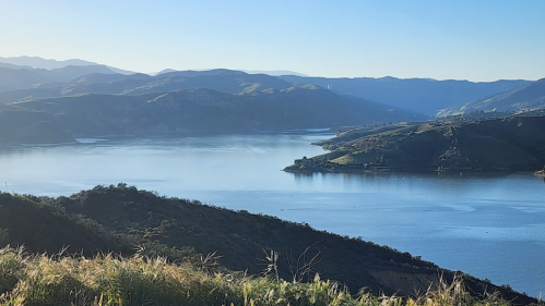 A serene landscape featuring a calm lake surrounded by mountains under a clear blue sky.