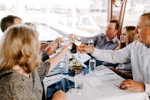 A group of people toasting with glasses at a dining table on a boat, enjoying a meal together.