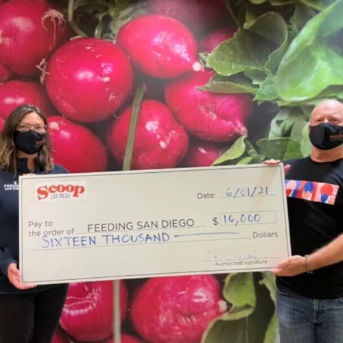 Two people hold a large check for $16,000 made out to Feeding San Diego, with a backdrop of green leaves and radishes.