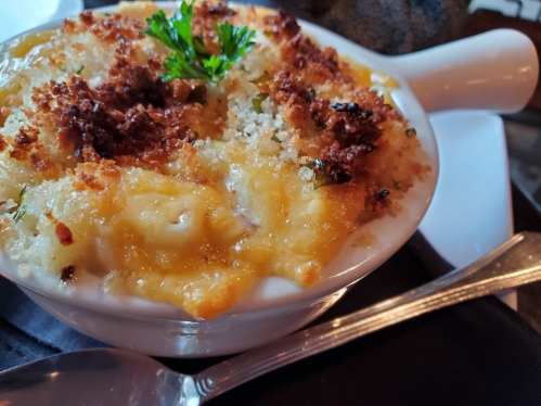 Creamy baked macaroni and cheese topped with golden breadcrumbs and a sprig of parsley, served in a white dish.