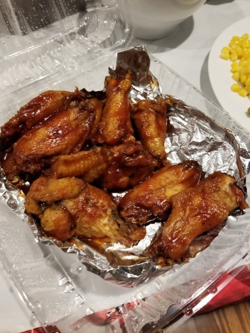 A tray of glazed chicken wings, arranged neatly on a foil-lined container.