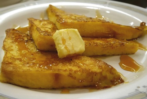 Three slices of French toast topped with a pat of butter and drizzled with syrup on a white plate.