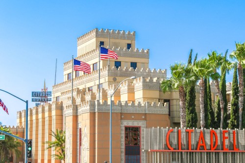 A colorful building resembling a castle, featuring flags and palm trees, with a sign reading "CITADEL" in the foreground.