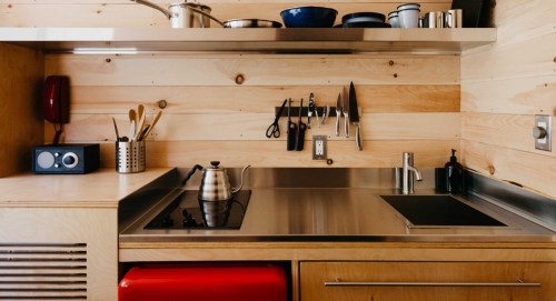 Modern kitchen with wooden walls, stainless steel countertop, kettle, utensils, and a red fridge.