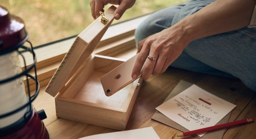 A person places a smartphone into a wooden box, with a lantern and notes on the floor nearby.