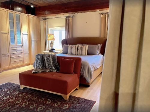 Cozy bedroom featuring a large bed, stylish decor, a plush bench, and warm wooden accents.