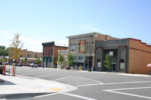 A sunny street view of a small town with historic buildings, shops, and trees lining the sidewalk.