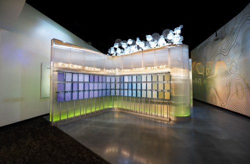 A modern installation featuring a wall of mailboxes with the phrase "Every scent takes you somewhere" illuminated above.