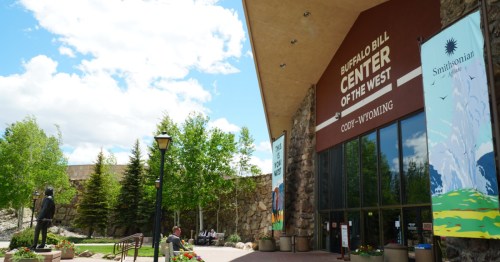 Exterior view of the Buffalo Bill Center of the West in Cody, Wyoming, featuring greenery and a statue.