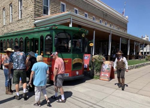 A colorful trolley parked outside a historic building, with people boarding and a man in period costume nearby.