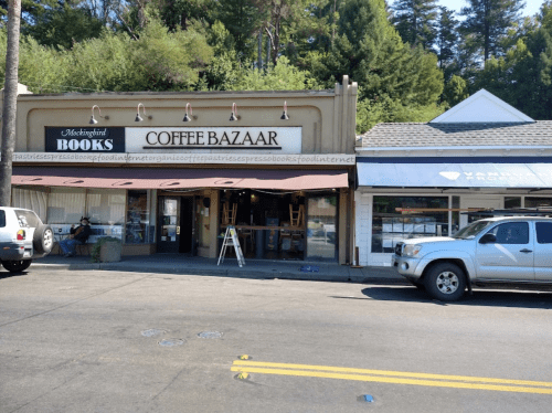 A storefront featuring "Coffee Bazaar" and "Books" signs, with outdoor seating and parked cars in front.