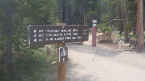 Trail signpost indicating junctions for Colorado Trail, Continental Divide Trail, and Mount Elbert Trail in a forested area.