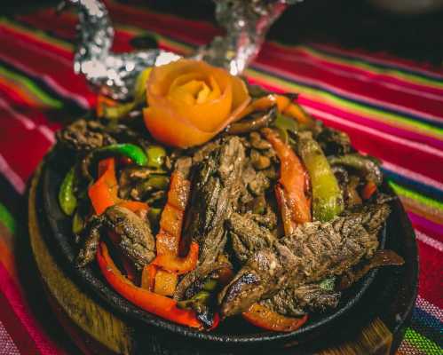 Sizzling beef fajitas with colorful bell peppers, served on a wooden platter, garnished with a rose made of carrot.