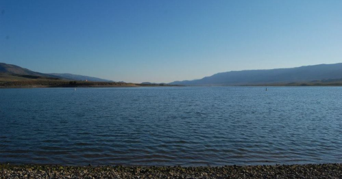 A serene lake surrounded by mountains under a clear blue sky, with calm water reflecting the landscape.