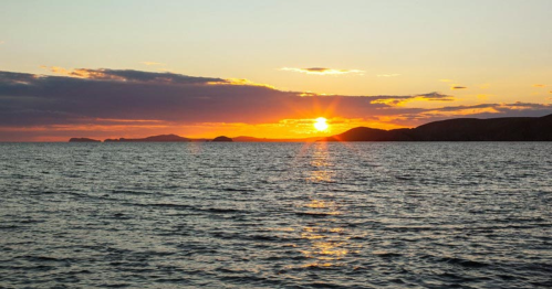 A serene sunset over the ocean, with silhouettes of distant islands against a colorful sky.