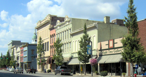 A charming street lined with colorful historic buildings and shops, under a blue sky with fluffy clouds.