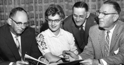 Four people, two men and two women, engaged in discussion while looking at a document or magazine.
