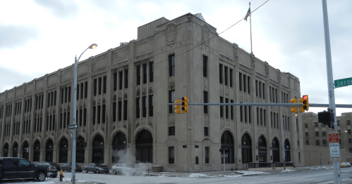 Historic building with a stone facade, large windows, and an American flag, set on a snowy street corner.