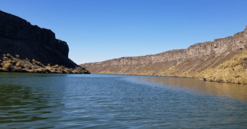 A serene river flows between steep, rocky cliffs under a clear blue sky.
