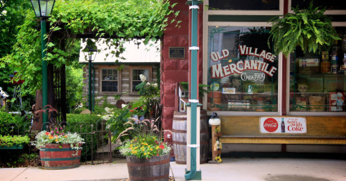 Charming storefront of "Old Village Mercantile" with greenery, flowers, and rustic decor.