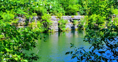 A serene lake surrounded by lush greenery and rocky cliffs under bright sunlight.