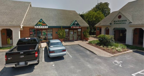A bakery and financial office in a small shopping plaza, with parked cars in front and greenery around.