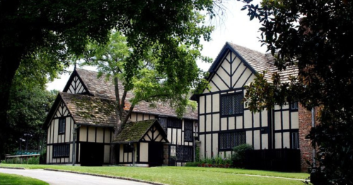 A picturesque scene of traditional Tudor-style houses surrounded by lush greenery and a clear blue sky.
