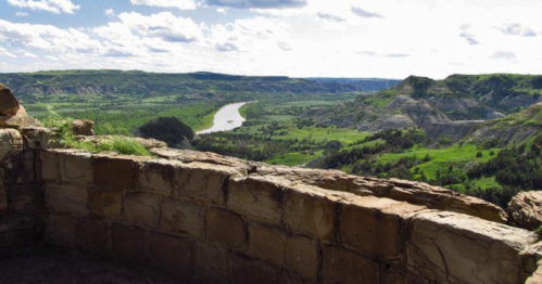 A scenic view of a river winding through lush green valleys and hills under a partly cloudy sky.