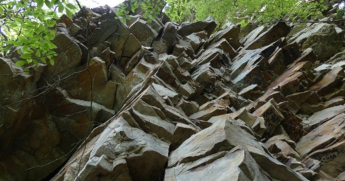A close-up view of a rugged rock face, showcasing jagged formations and greenery above.