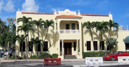 A yellow building with a tiled roof, palm trees, and a sign reading "Joe's" in a sunny outdoor setting.