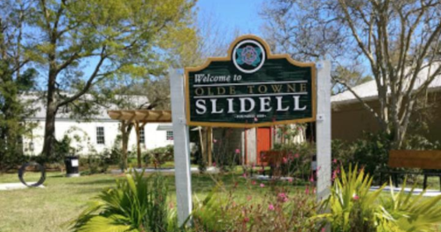 Welcome sign for Olde Towne Slidell, surrounded by greenery and trees on a sunny day.