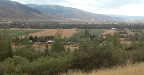 A scenic view of rolling hills and farmland, with trees and fields under a cloudy sky.