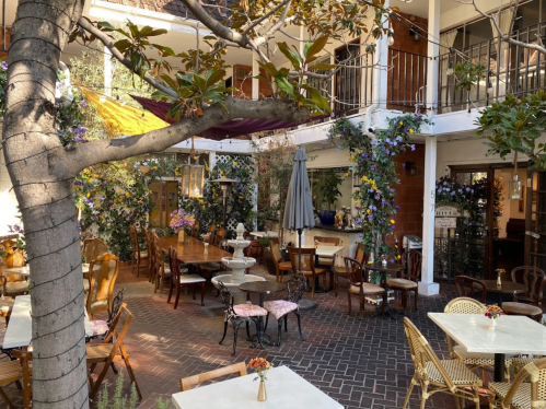 Charming outdoor café with wooden tables, chairs, and lush greenery, creating a cozy and inviting atmosphere.