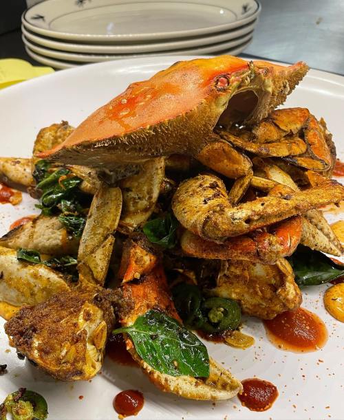 A plate of spicy crab with vibrant greens and sauce, garnished with sliced jalapeños, served on a white dish.