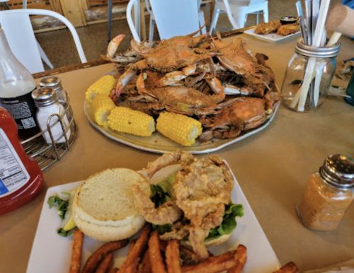 A platter of crabs with corn on the cob, alongside a plate of fried chicken and sweet potato fries.