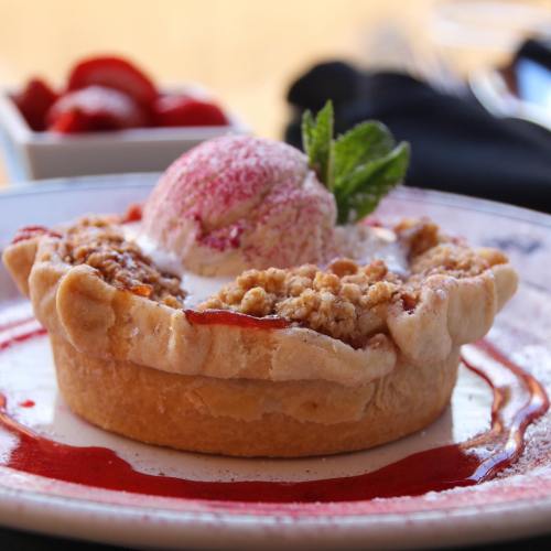 A delicious strawberry pie topped with a scoop of pink ice cream and a mint leaf, served on a decorative plate.