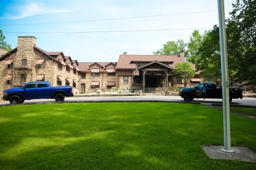 Two blue trucks parked in front of a large stone lodge surrounded by green grass and trees on a sunny day.